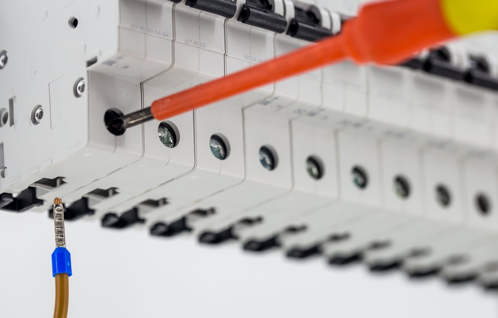 An electrician torque-checking a ferrule termination on a row of DIN-rail circuit breakers